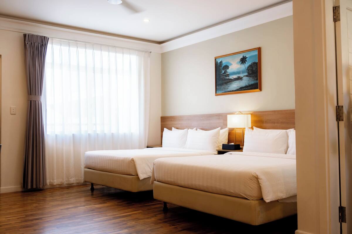 Une chambre d’hôtel avec deux lits, un tableau au mur et une fenêtre avec des rideaux.