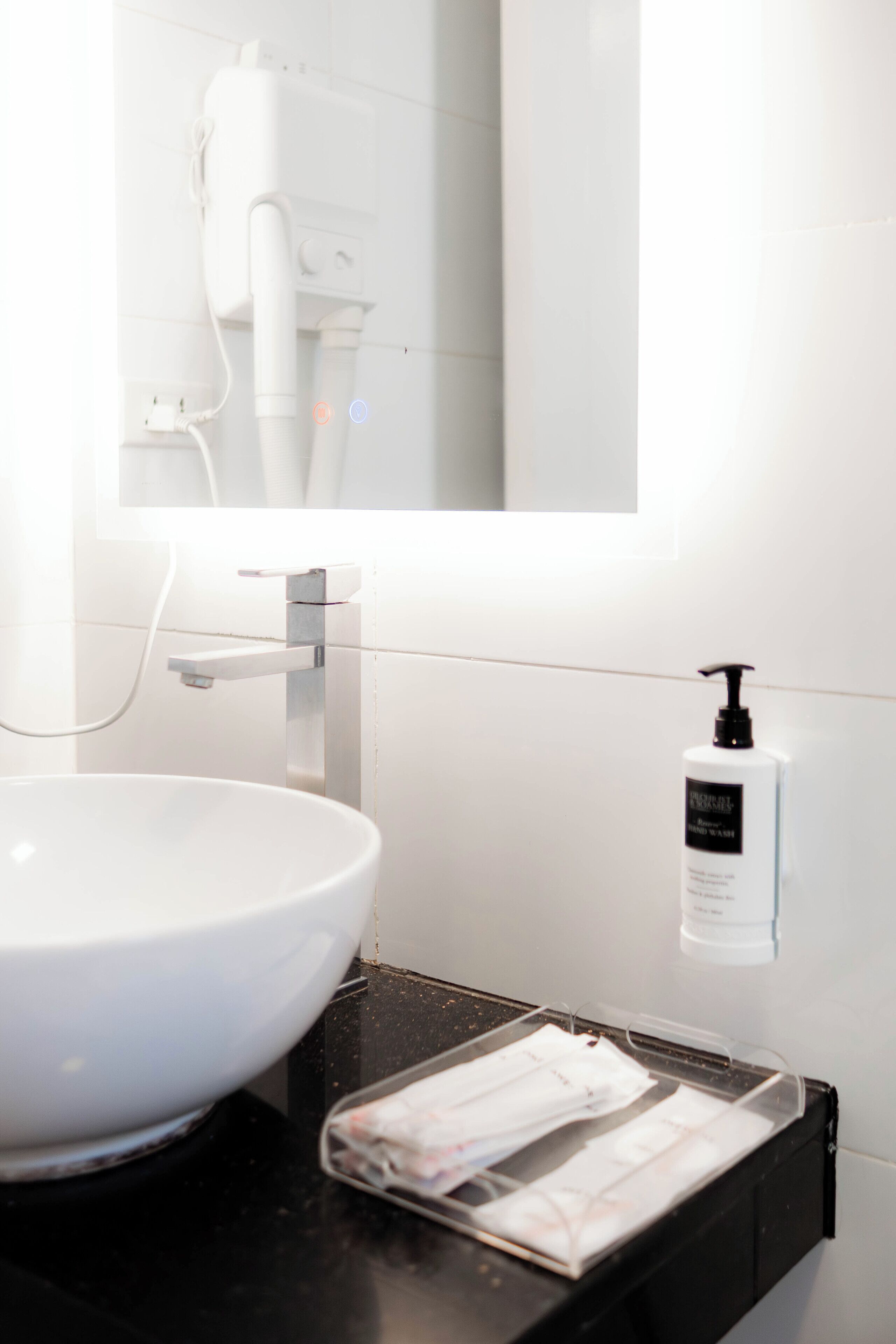 Een badkamer met een witte wastafel, een spiegel, een handdouche en een fles shampoo aan de muur.