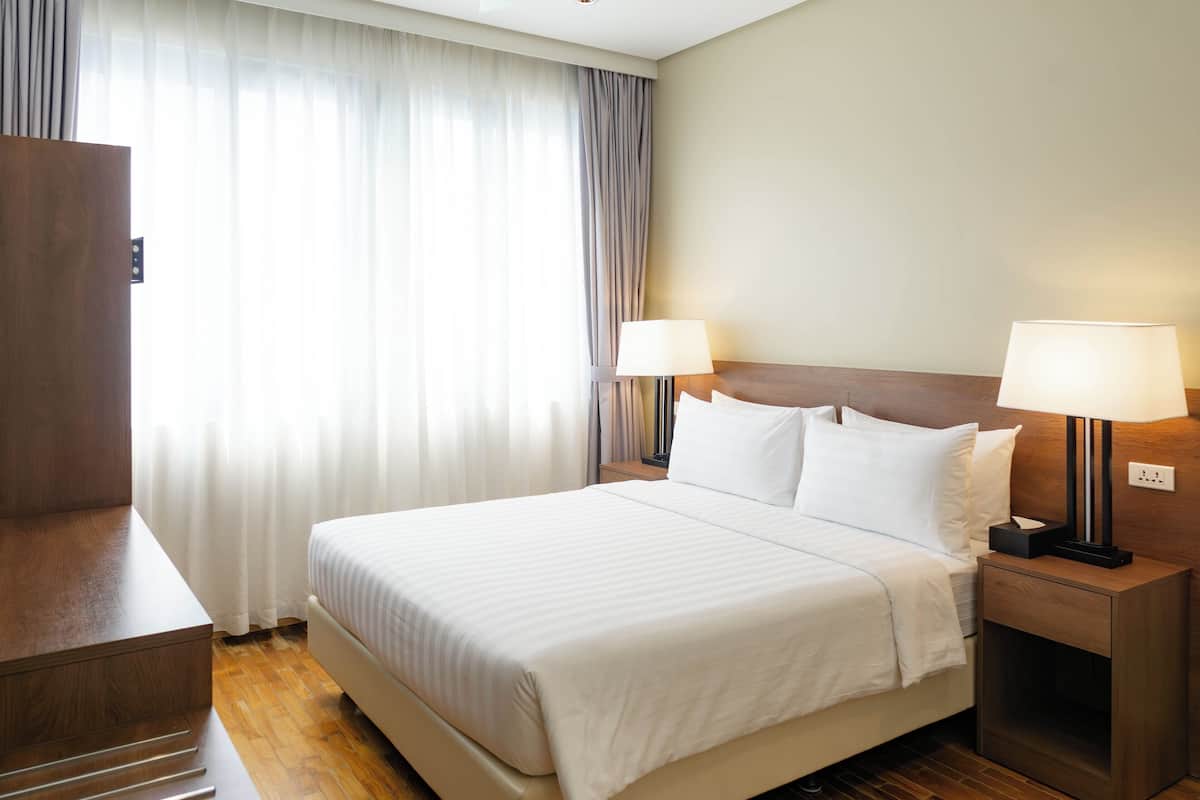 Une chambre d’hôtel avec un lit, deux lampes de chevet, une table de nuit en bois et une grande fenêtre avec des rideaux.
