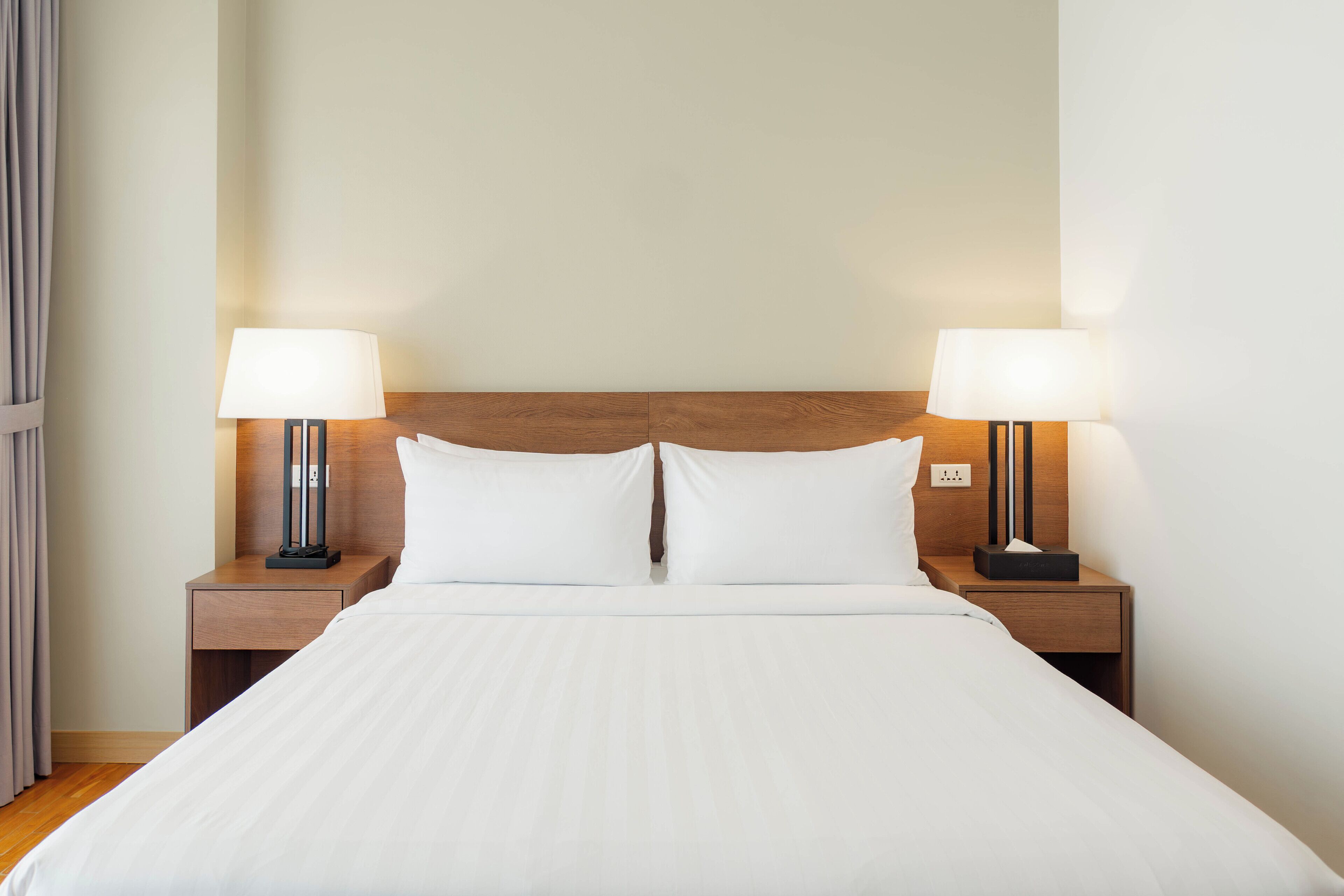 A neatly made bed with white linens, two bedside lamps, and a wooden headboard.
