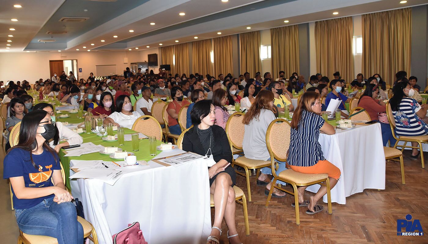 Un salón de conferencias con mesas redondas, asistentes sentados y un escenario al frente.
