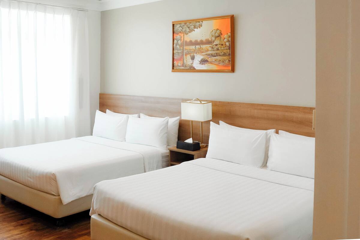 Une chambre d’hôtel avec deux lits, une tête de lit en bois, une table de chevet avec une lampe et un tableau au mur.