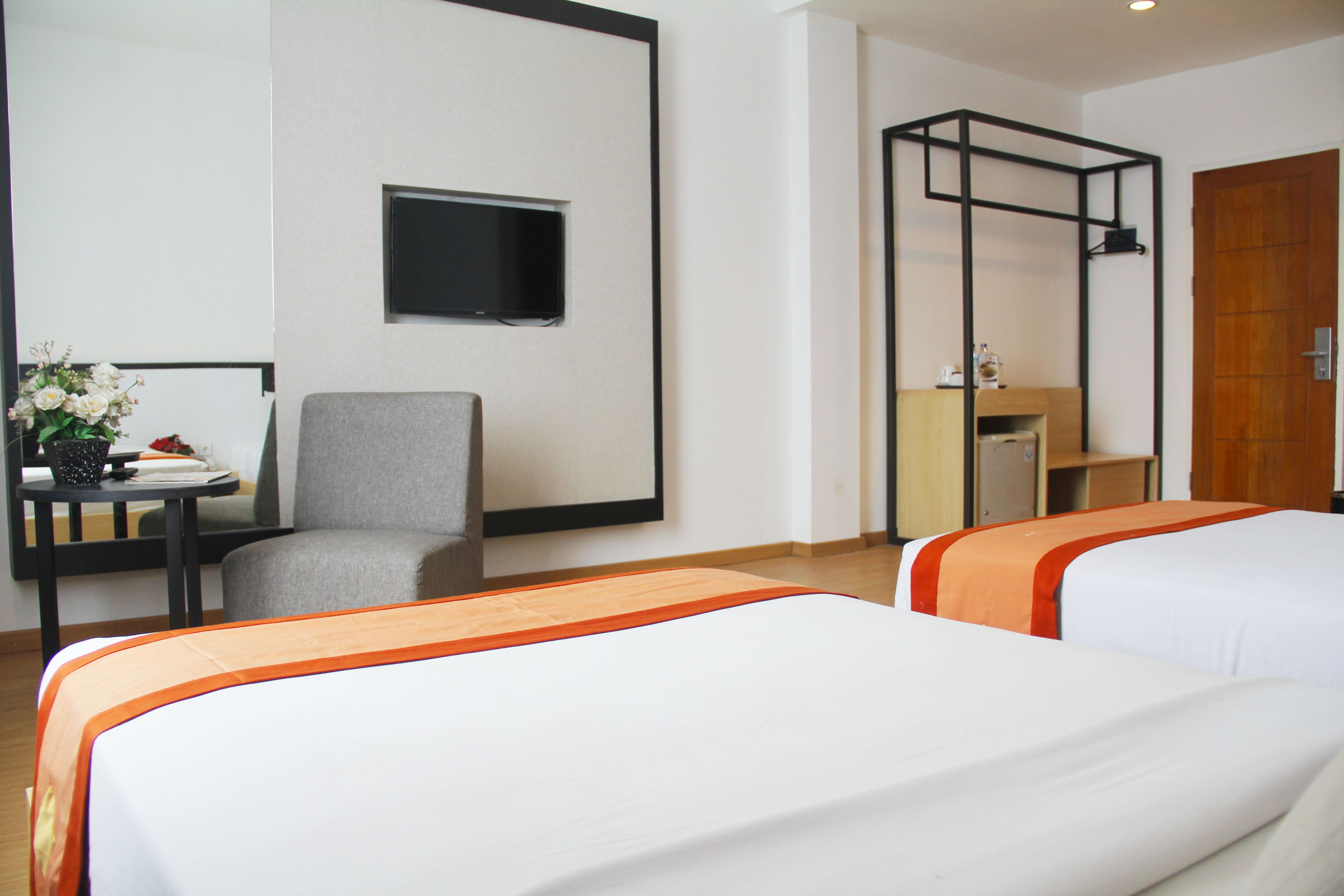 Een hotelkamer met twee bedden, een bureau, een stoel, een aan de muur bevestigde televisie en een houten deur.