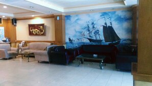 A lobby with a large mural of a sailing ship, plush seating, and a tiled floor. - Hotel Buana Lestari (Balikpapan)