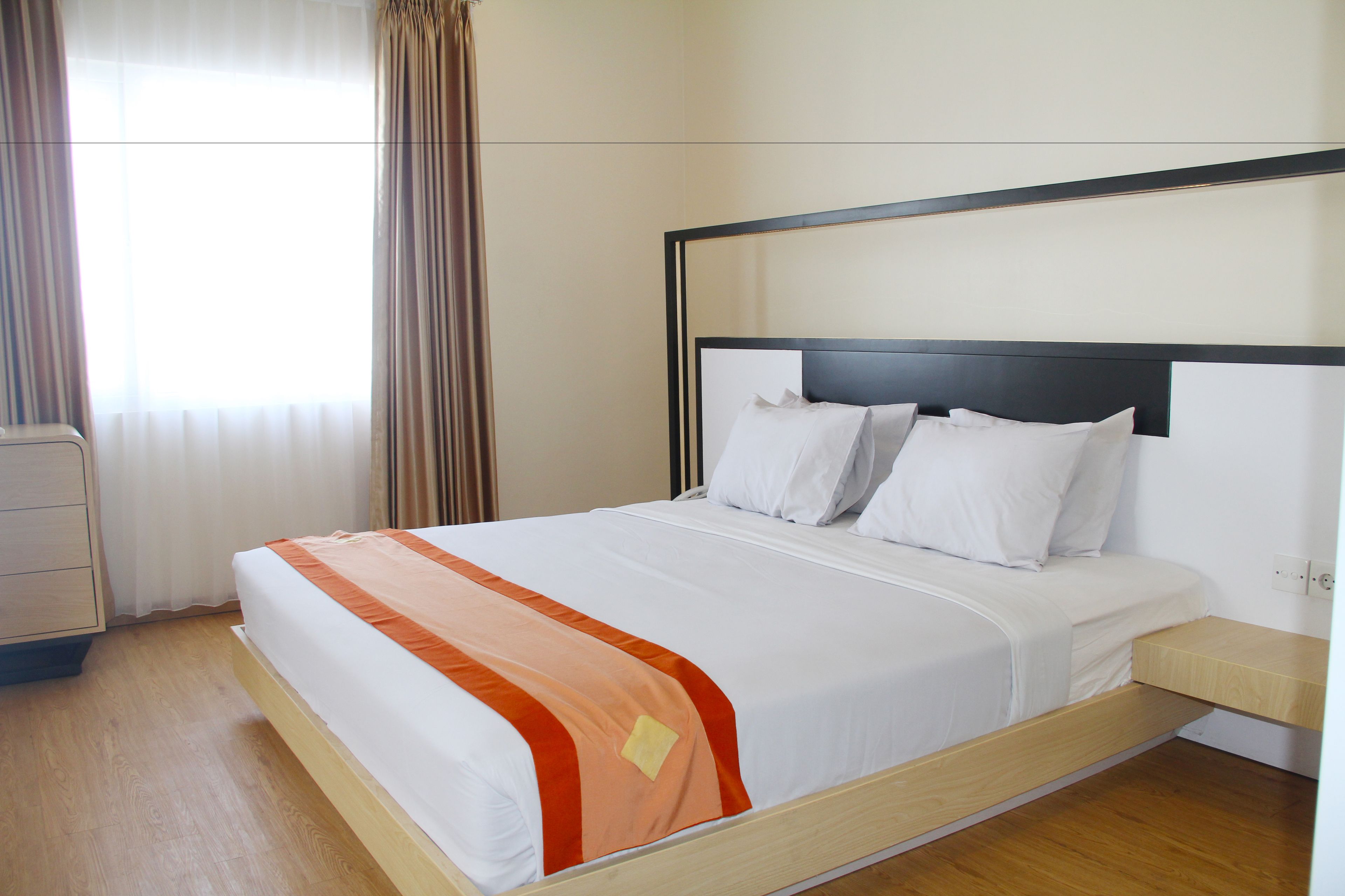 Una cama bien tendida con ropa blanca y naranja, un cabecero de madera y una mesita de noche.