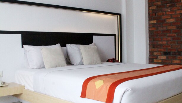 A modern hotel room with a large bed, a wooden headboard, and a brick accent wall. - Hotel Buana Lestari (Balikpapan)