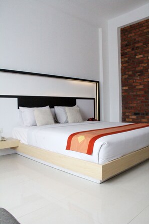 A modern hotel room with a large bed, a wooden headboard, and a brick accent wall.