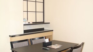 A dining area with a dark wooden table and matching chairs, a built-in bench, and a small kitchen area above the table. - Hotel Buana Lestari (Balikpapan)