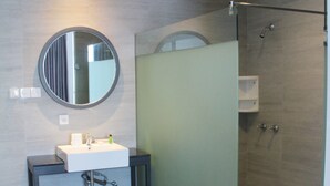 A modern bathroom with a round mirror, a white sink, and a glass shower enclosure. - Hotel Buana Lestari (Balikpapan)
