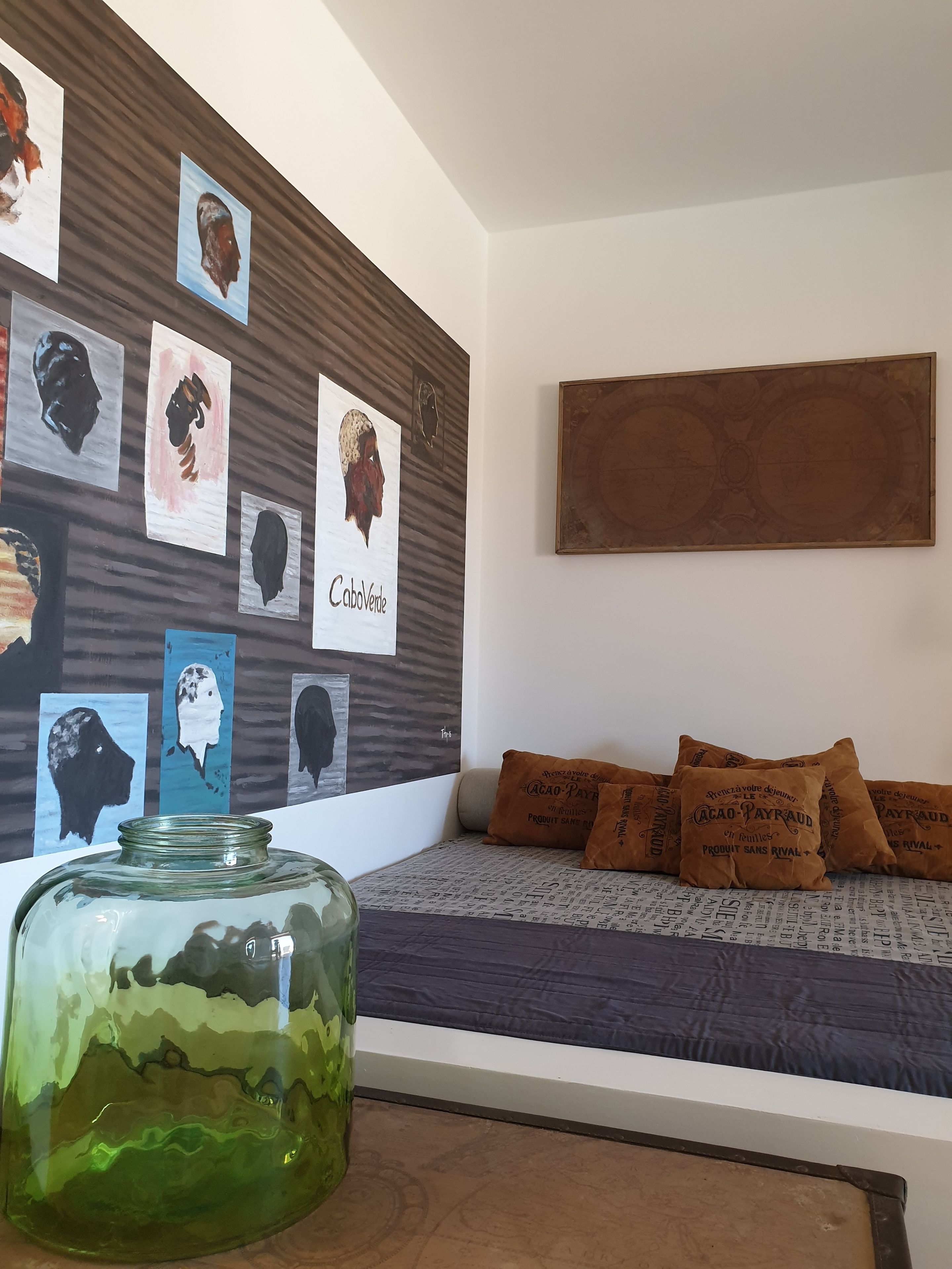 Una habitación con una cama, una pared decorada con obras de arte y un tarro de vidrio con un diseño de paisaje.