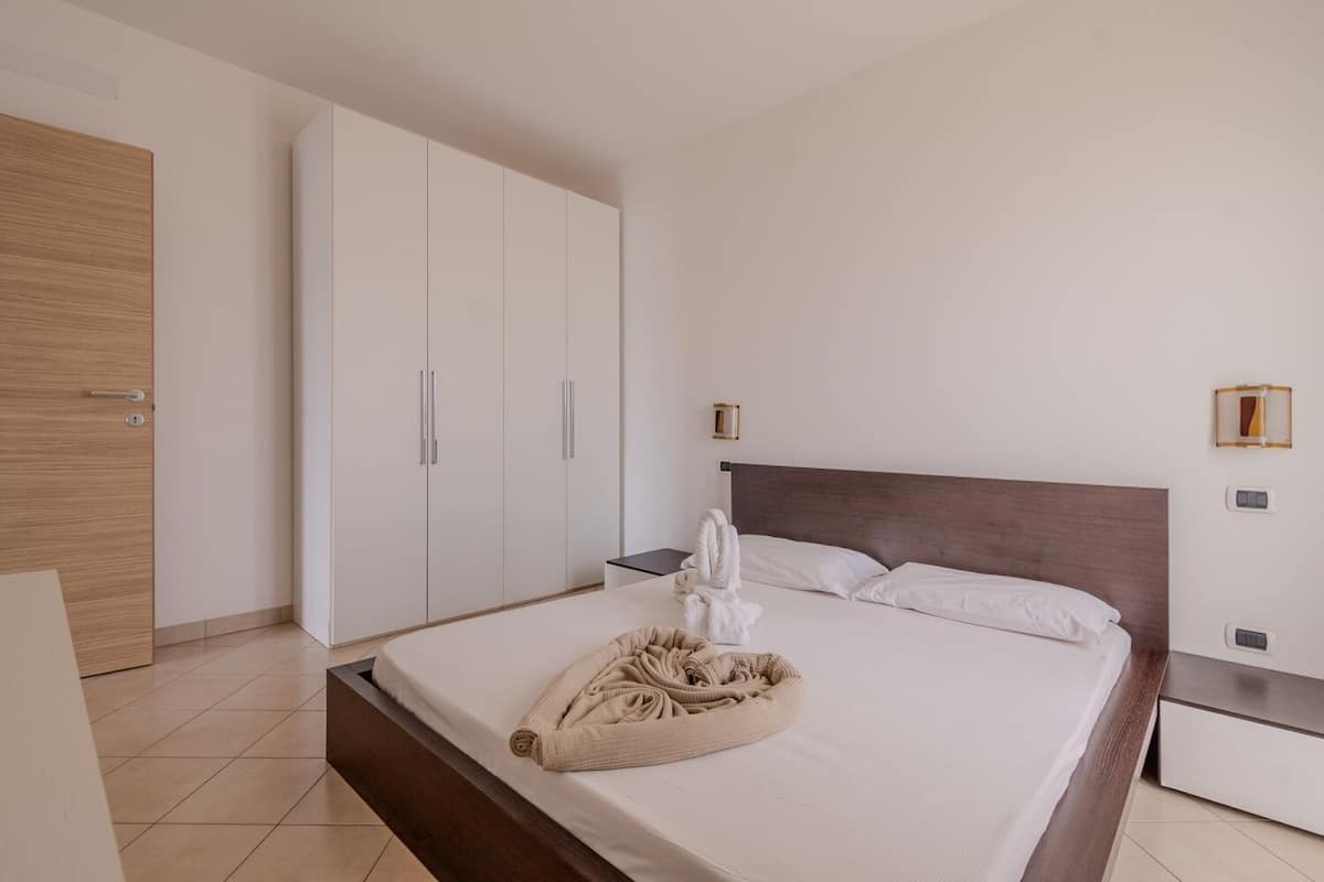 Ein Hotelzimmer mit Bett, Holzschrank, Nachttisch und Wandlampe.