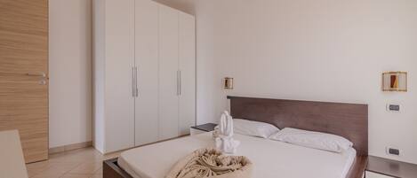 A hotel room with a bed, a wooden wardrobe, a nightstand, and a wall-mounted light fixture.