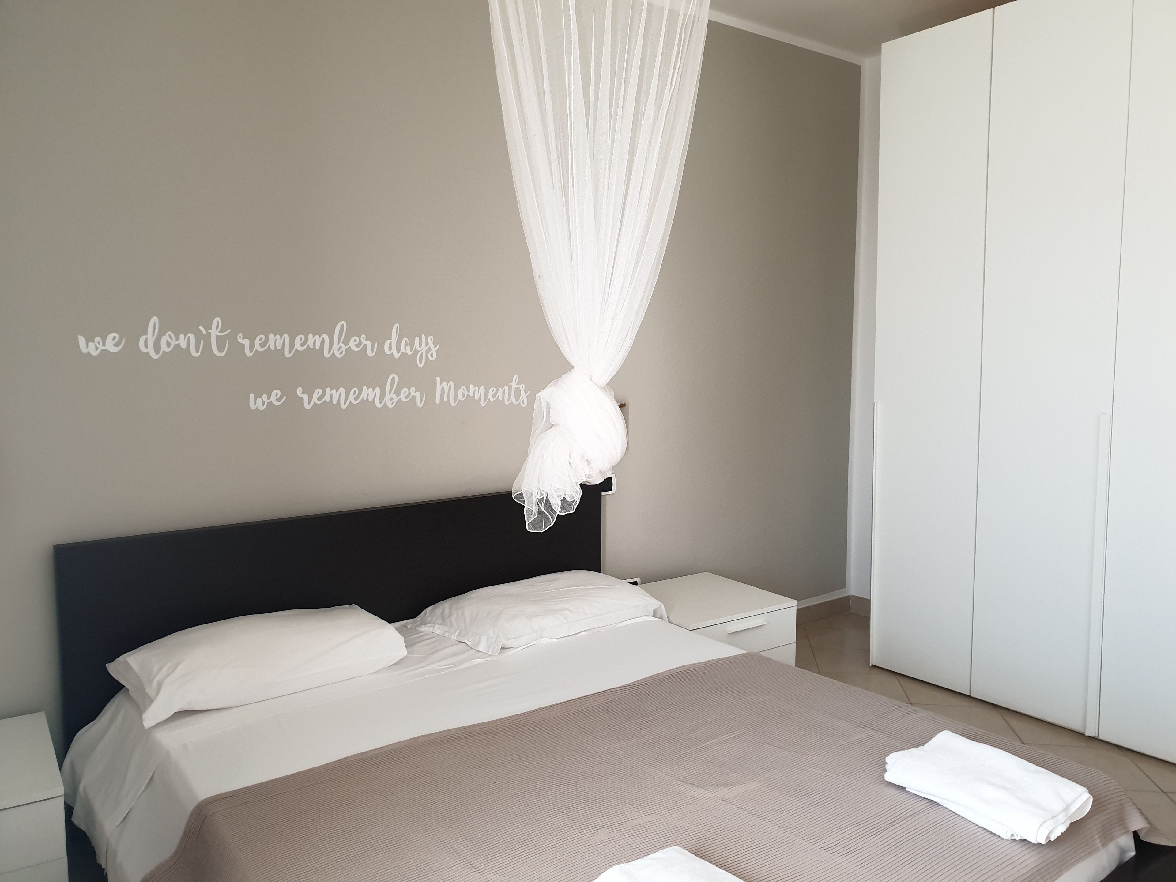 A bedroom with a bed, a bedside table, a wardrobe, and a wall with a motivational quote.