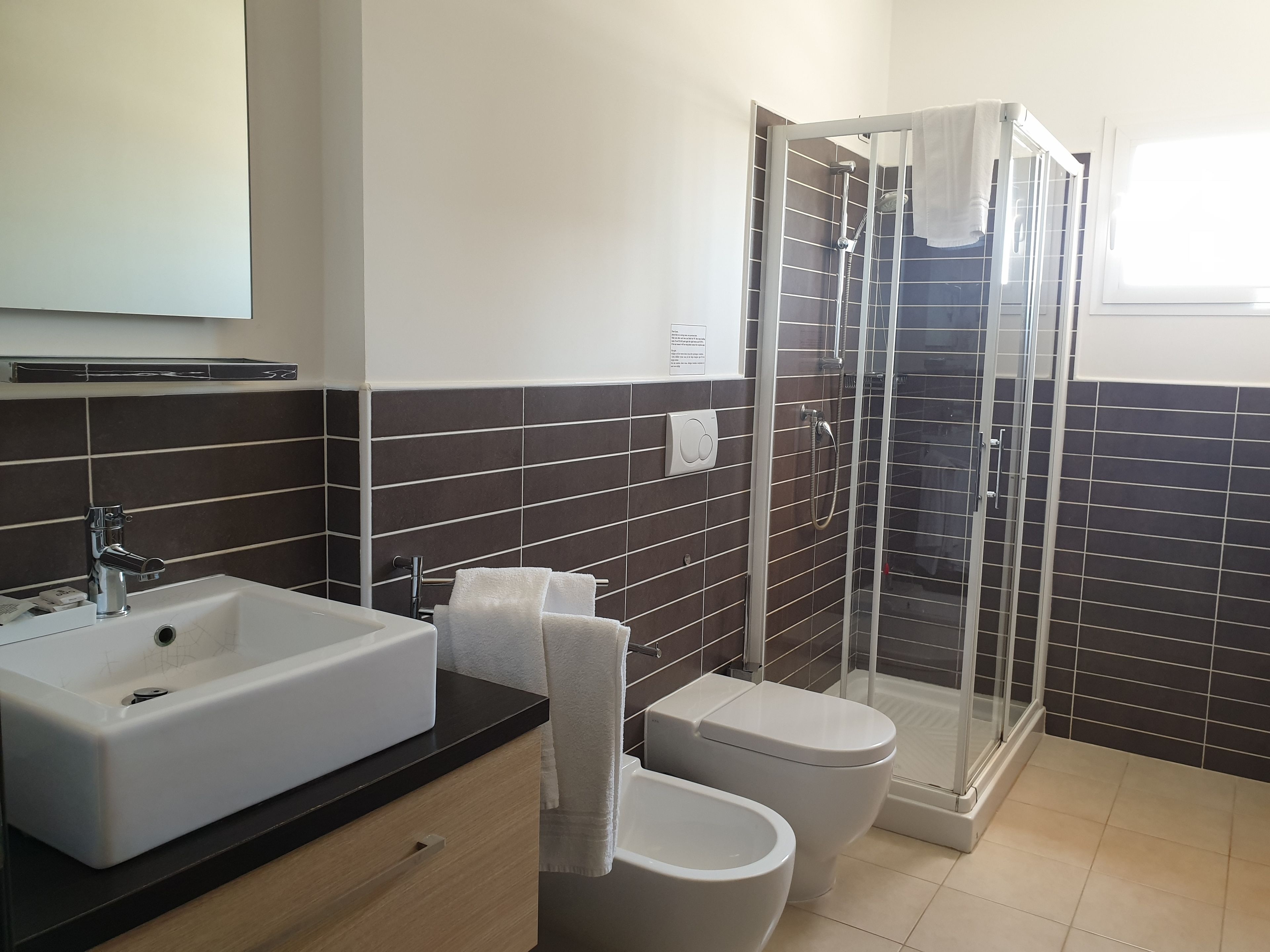 A modern bathroom with a large white sink, a toilet, and a glass-enclosed shower area.