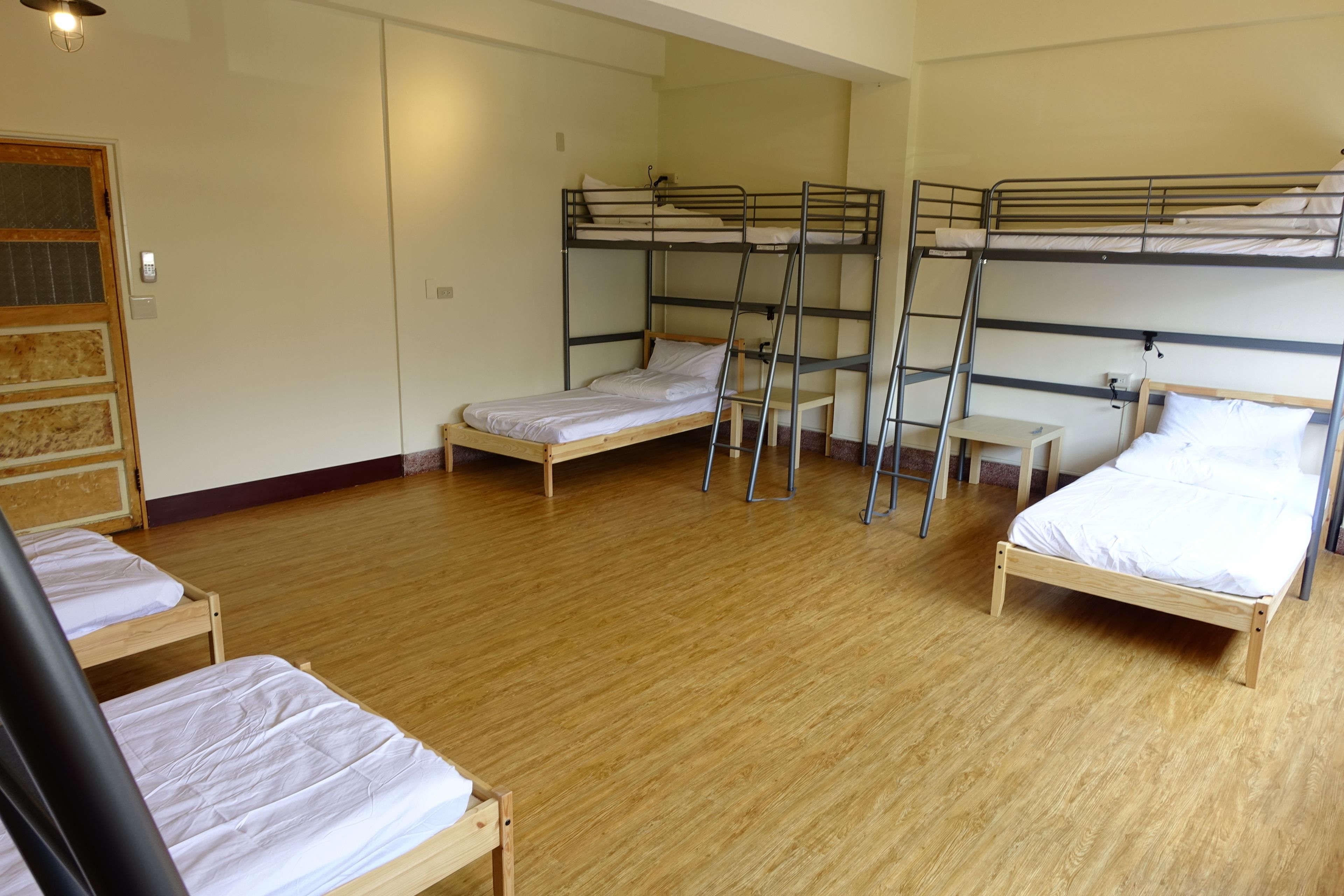 A dormitory room with bunk beds, wooden floors, and a door with a window.