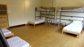 A dormitory room with bunk beds, wooden floors, and a door with a window.