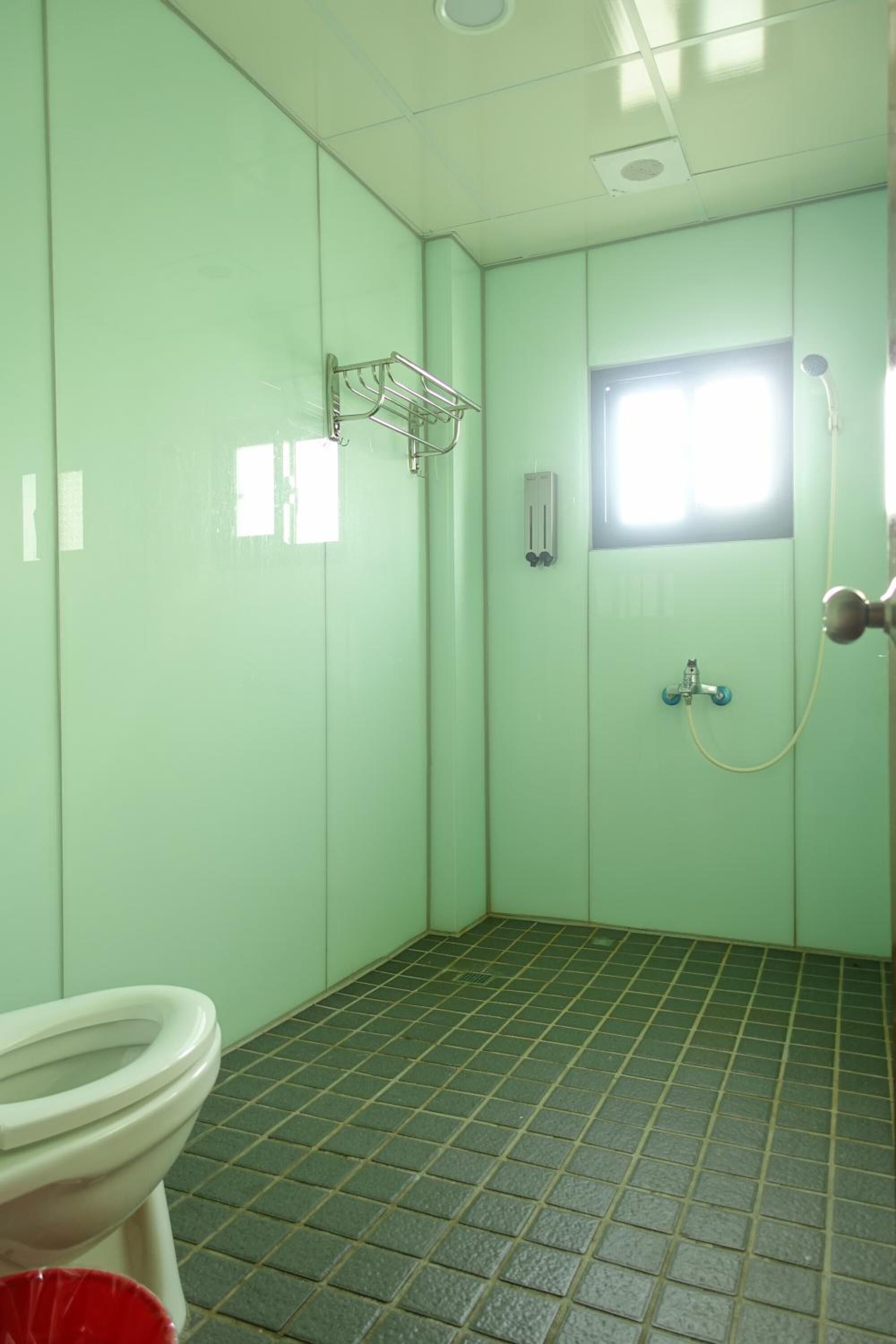 A small, private bathroom with a toilet, a shower, and a window.