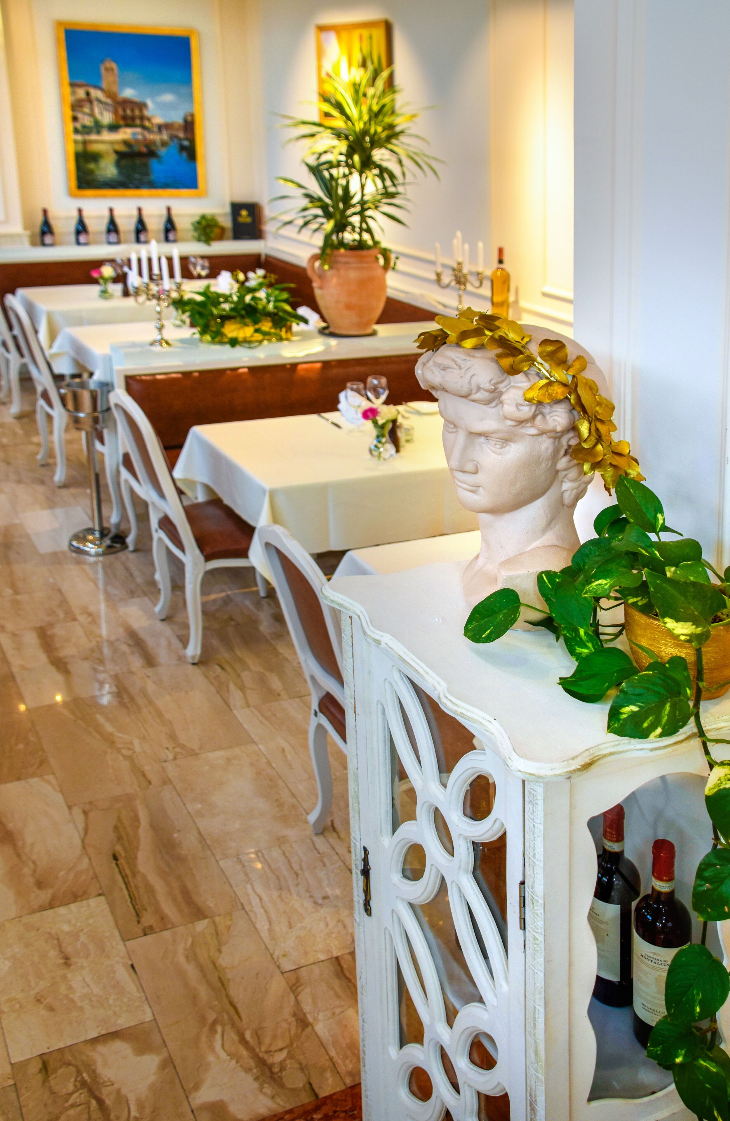 Un restaurante con mesas y sillas blancas, y un mueble decorativo blanco con botellas de vino.