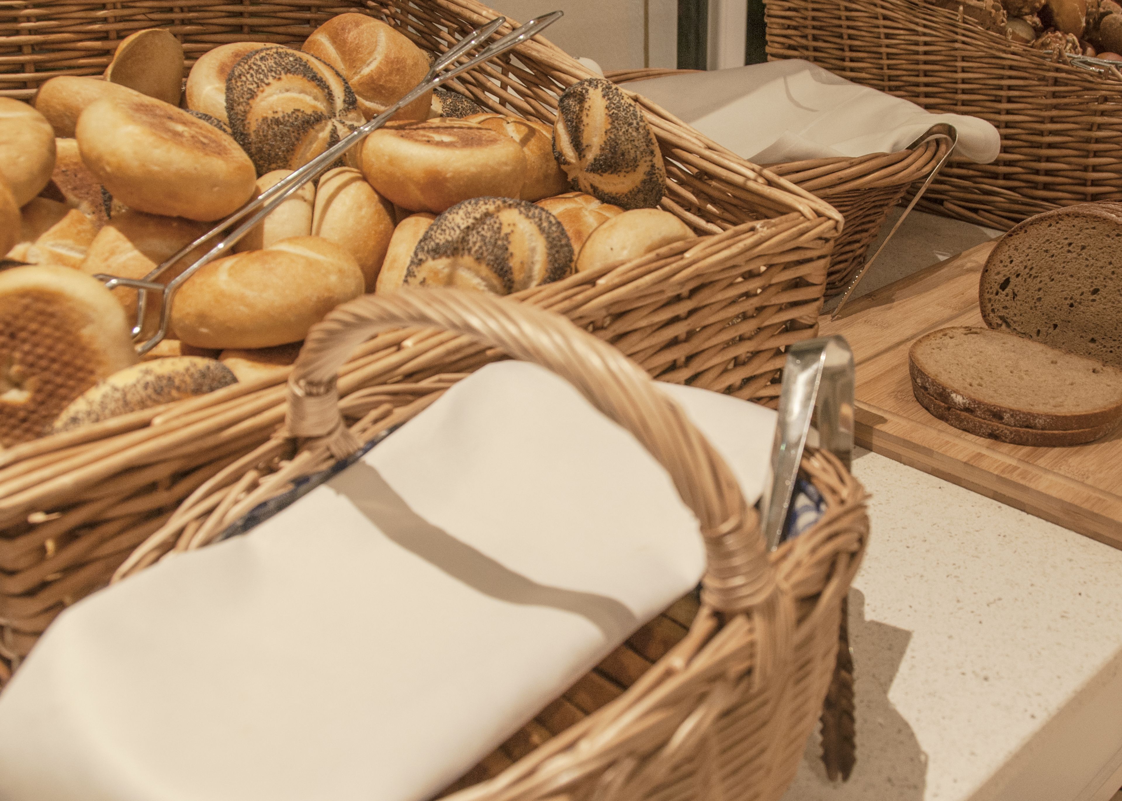 Cestas de mimbre llenas de panes variados y una tabla con pan rebanado.