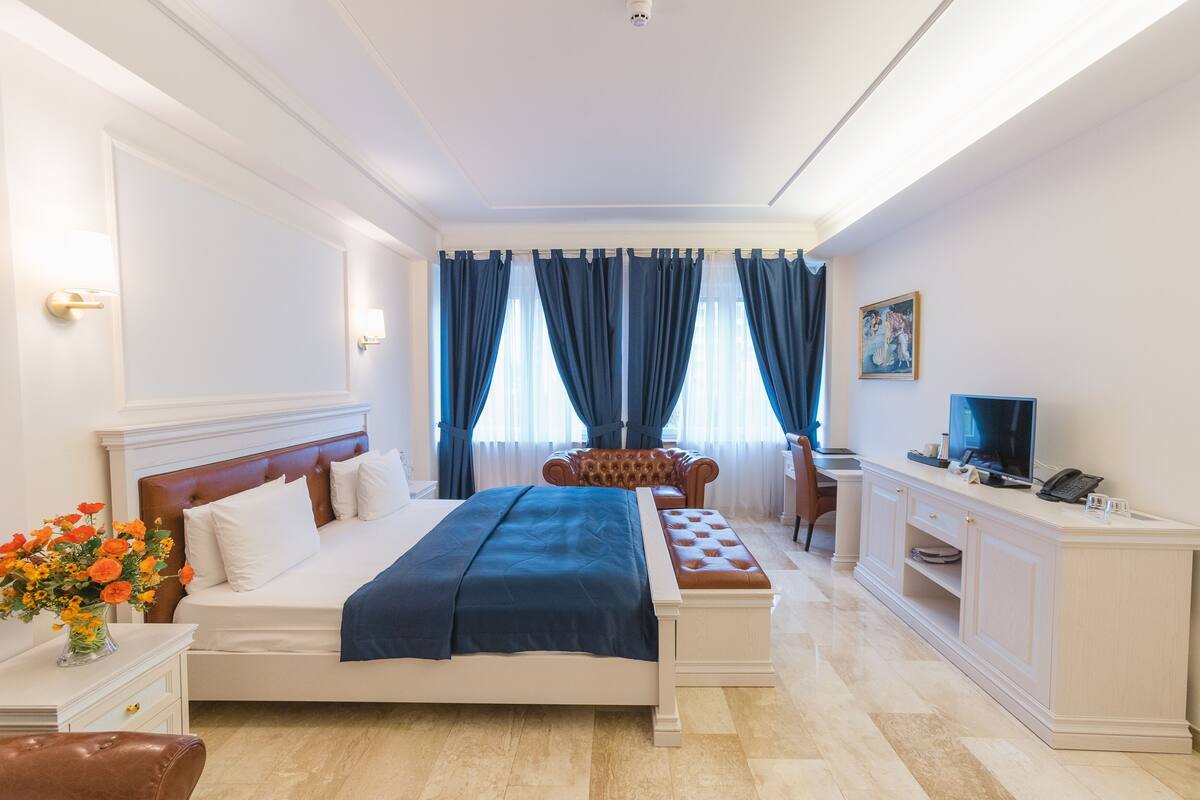 A hotel room with a large bed, a desk with a computer, a chair, and a TV.