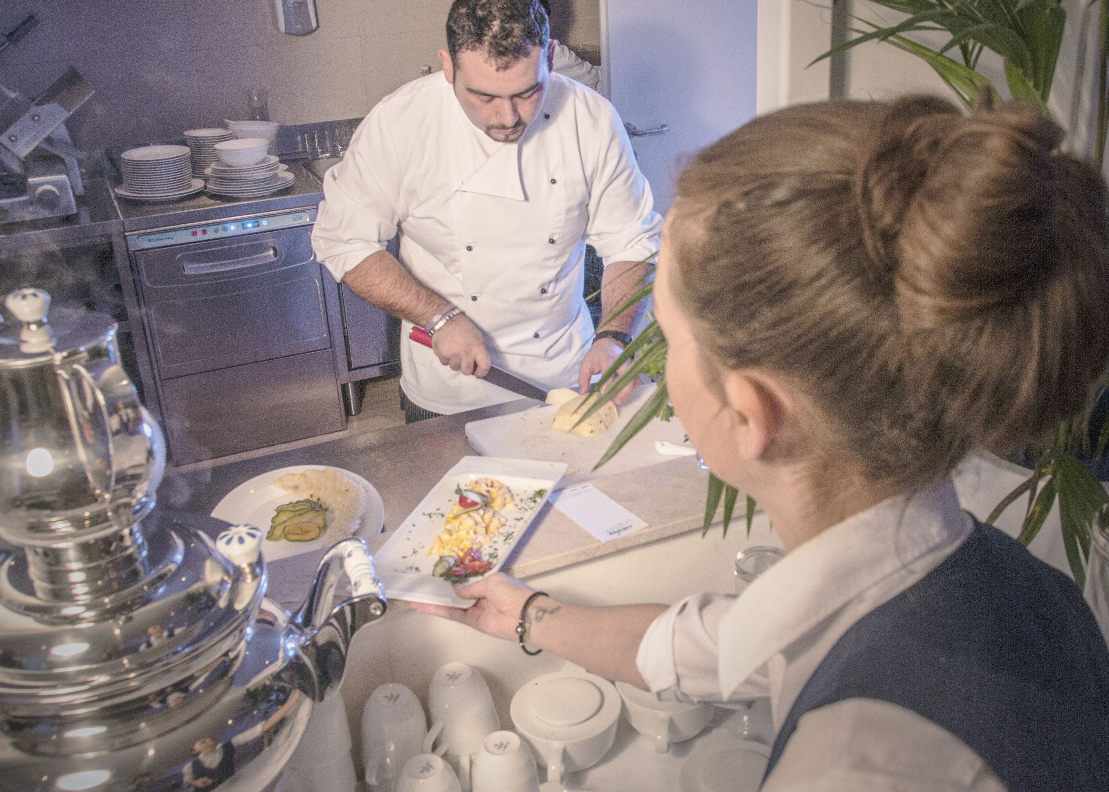 Un chef prepara comida en una cocina con electrodomésticos de acero inoxidable y un lavamanos.