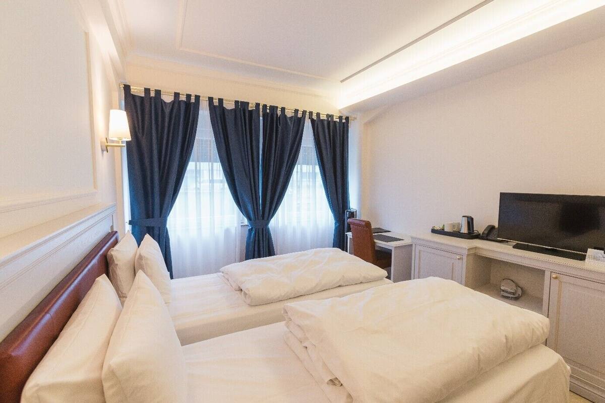 A hotel room with two beds, a desk with a TV, and a window with curtains.