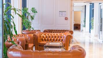 Eine Lobby mit ledernen Sofas, die halbkreisförmig angeordnet sind, einer großen Topfpflanze und Blick auf einen Flur mit einer Tür.
