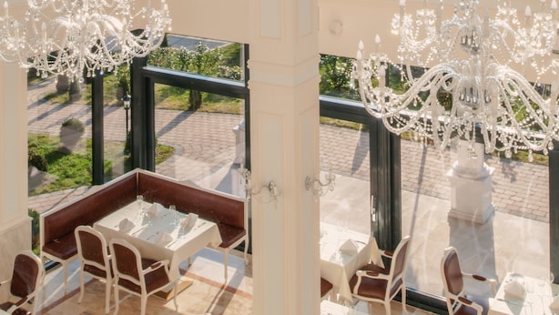 Un restaurant doté d’une terrasse, de tables et de chaises blanches, et d’un lustre.