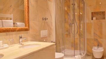 A modern bathroom with a marble vanity, a glass-enclosed shower, a bidet, and a toilet.