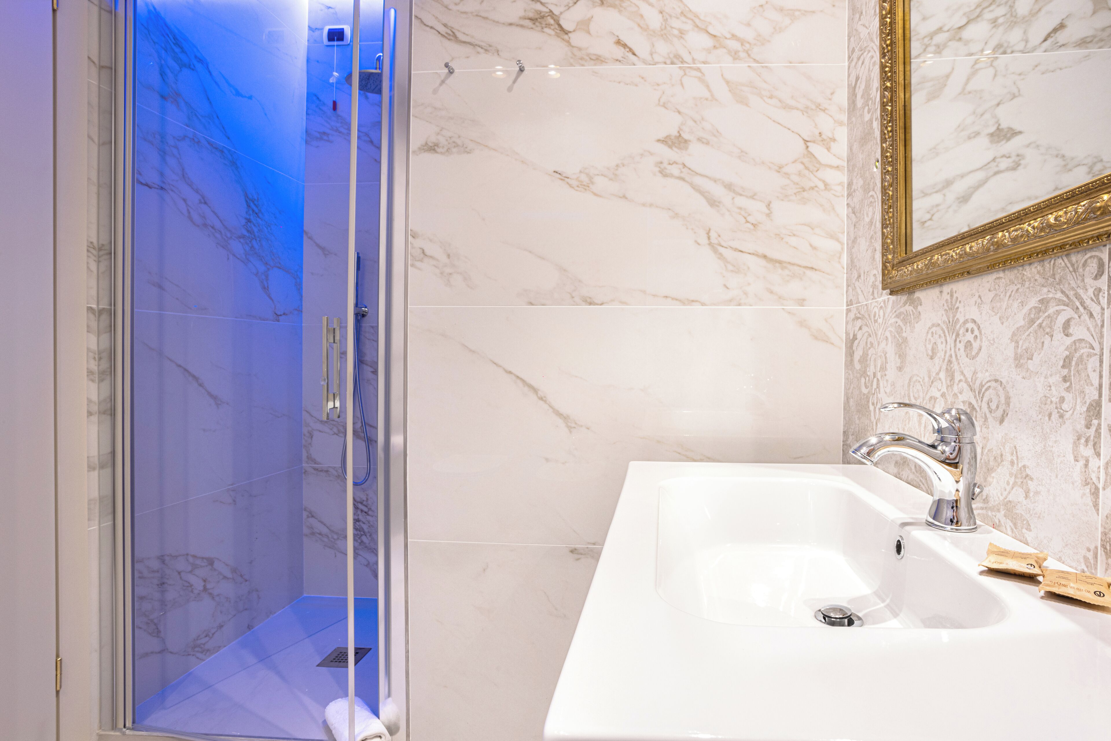 A bathroom with a glass-enclosed shower, a white sink, and a gold-framed mirror.
