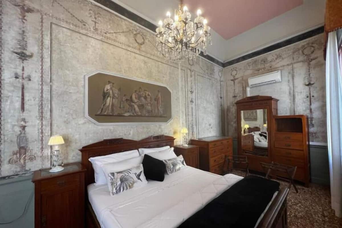 Ein Schlafzimmer mit einem großen Bett, Holzmöbeln, einem Chandelier und einem Wandgemälde.
