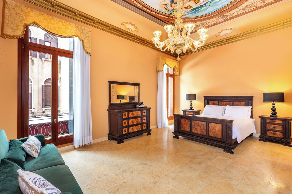 Ein Schlafzimmer mit einem großen Bett, einem Schminktisch, einem grünen Sofa und einer Deckenleuchte.