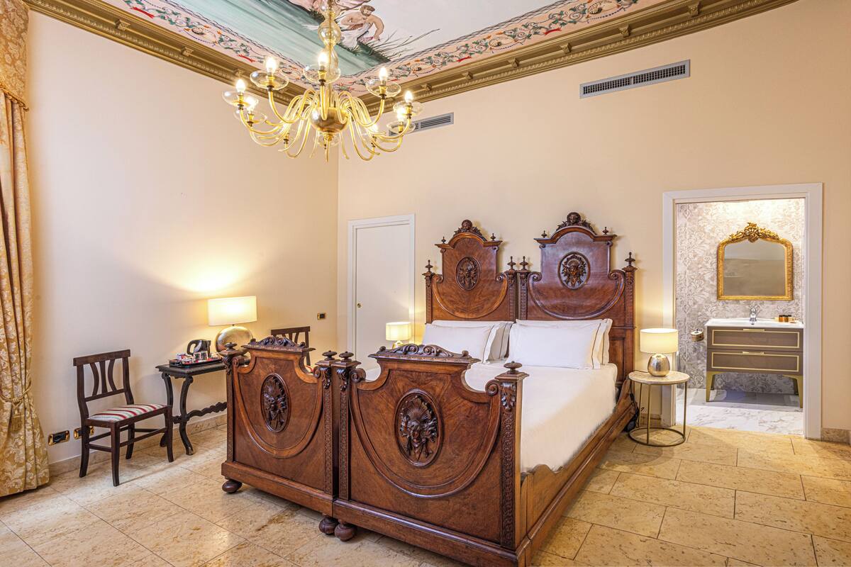 Ein geräumiges Schlafzimmer mit einem großen Bett, einem Kronleuchter, einem Schminktisch mit Spiegel und einer separaten Sitzecke mit Stuhl und Tisch.