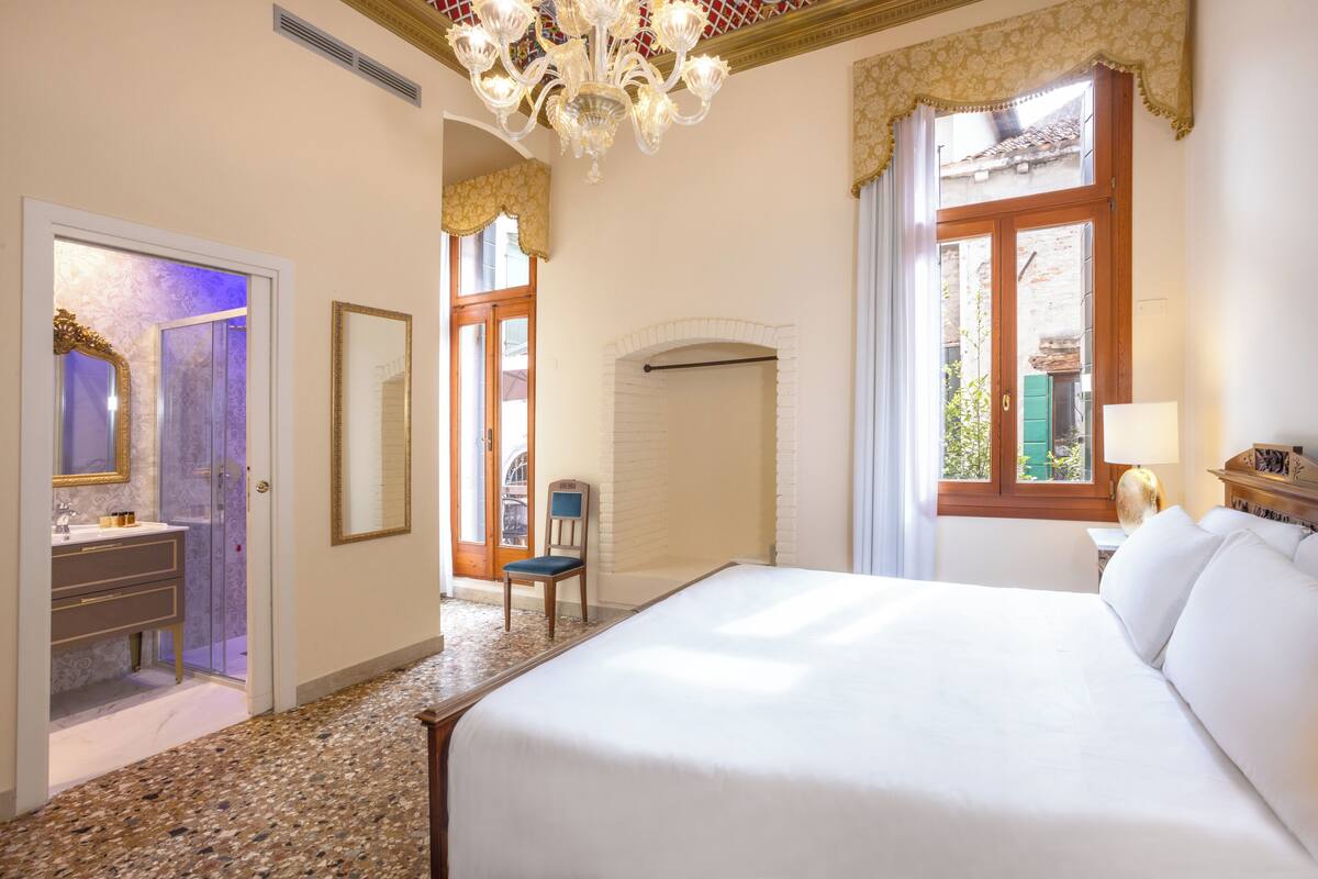 Ein Hotelzimmer mit einem großen Bett, einer Sitzecke mit einem Sessel, einem Schminktisch mit Spiegel und Blick durch ein Fenster nach draußen.