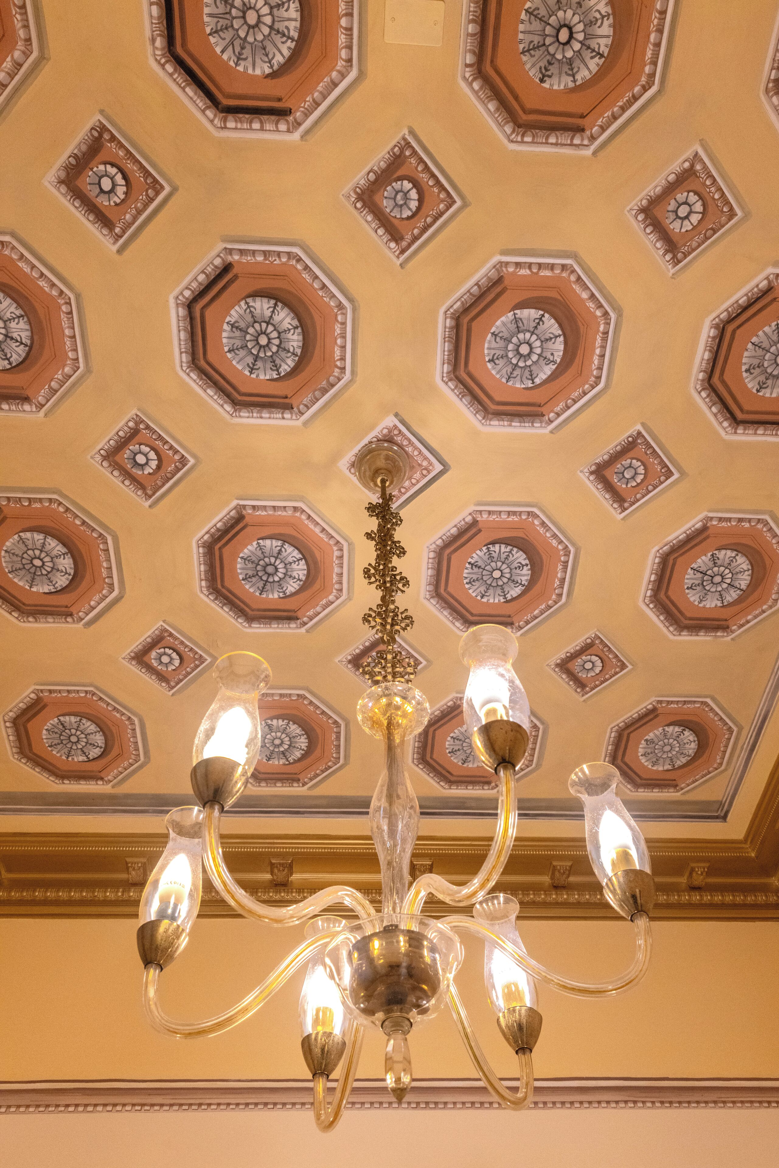 A chandelier with multiple light fixtures hanging from a ceiling with octagonal patterns.