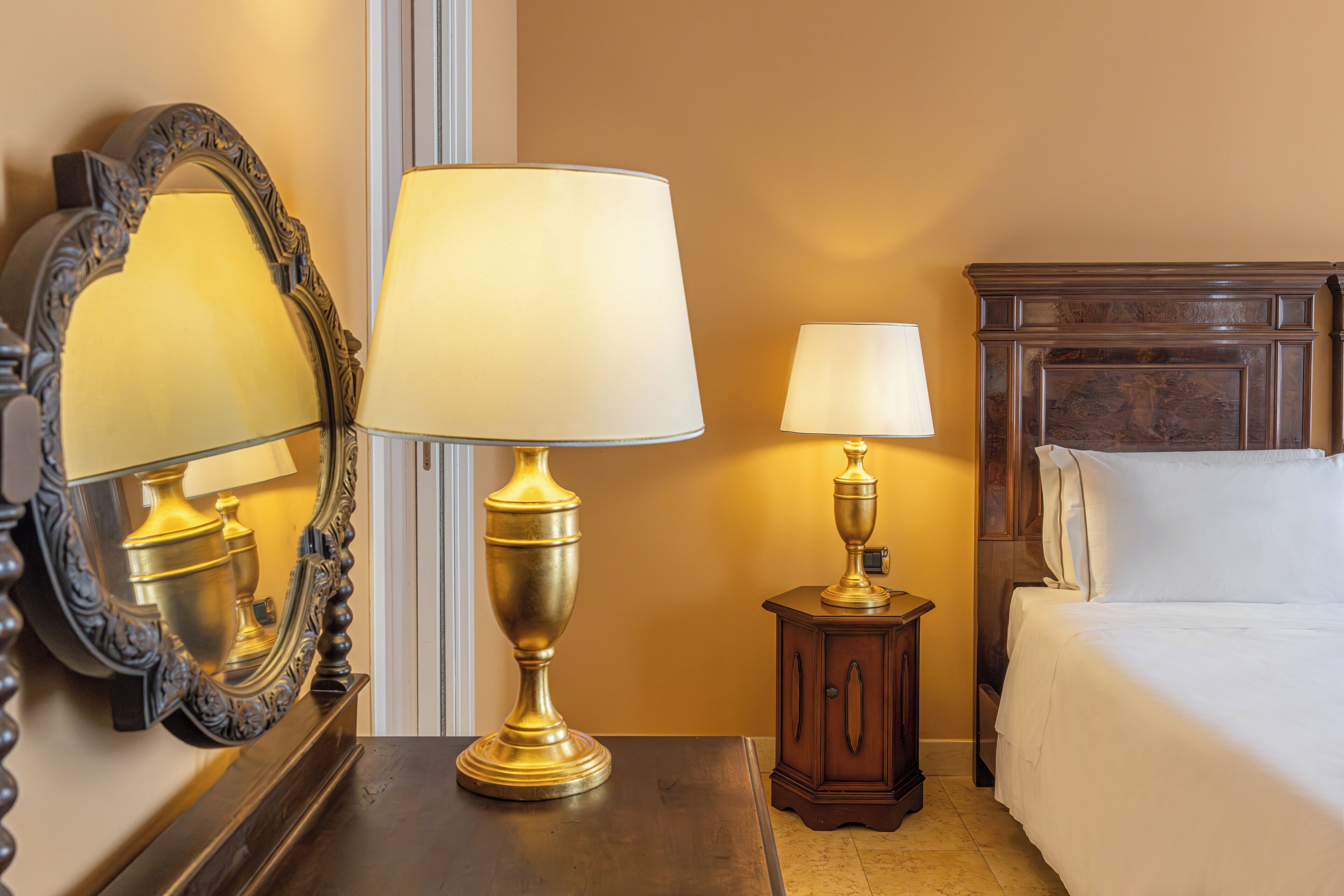 Une chambre d’hôtel avec un lit, deux lampes de chevet, un miroir et une table de chevet en bois.