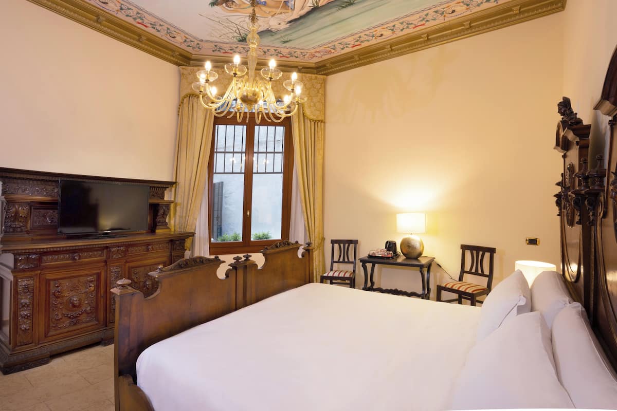 Ein Hotelzimmer mit einem großen Bett, einem Holzschrank, einem Fernseher, einer Kronleuchter und einem fenster mit Vorhängen.