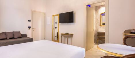 A hotel room with a large bed, a bedside table, a TV mounted on the wall, a small table with a chair, and a mirror.