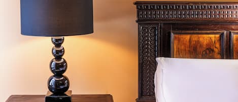 A wooden nightstand with a black lamp and a white pillow on a bed with a carved headboard.