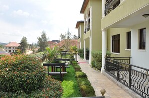 A pathway lined with benches and bordered by neatly trimmed hedges, leading to a building with balconies and columns. - Primebiz Apartments (Kigali)
