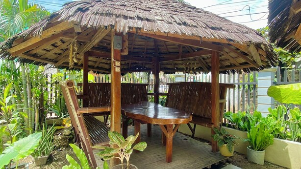 A wooden gazebo with a thatched roof, surrounded by potted plants and a tiled patio area. - Coron Vista Lodge (Coron)