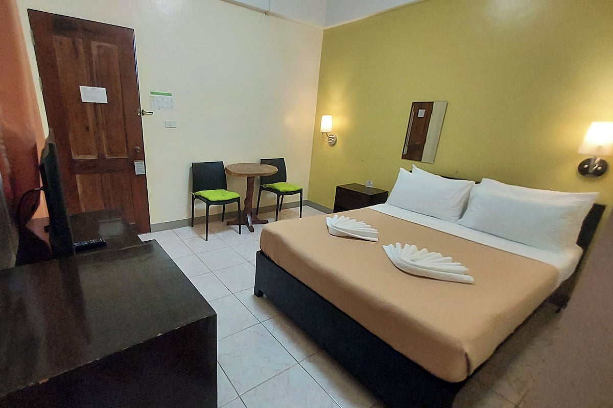 A hotel room with a bed, a desk, two chairs, a small table, and a nightstand.