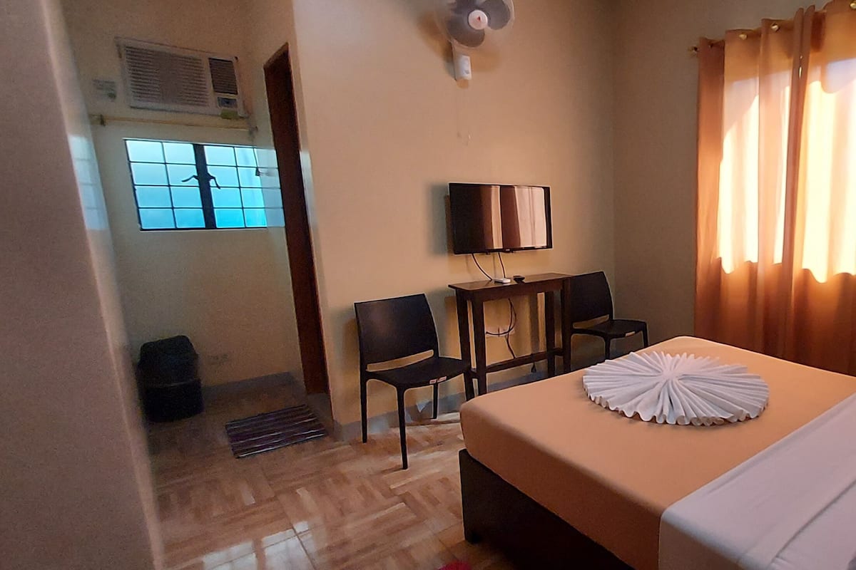 A hotel room with a bed, a desk, a chair, a TV, and a window with curtains.