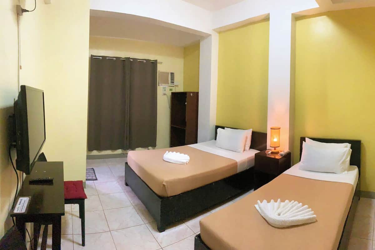 A hotel room with two beds, a desk, a television, and a nightstand with a lamp.
