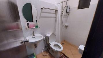 A small bathroom with a sink, toilet, and mirror. There is a shower curtain rod and a soap dispenser on the wall.