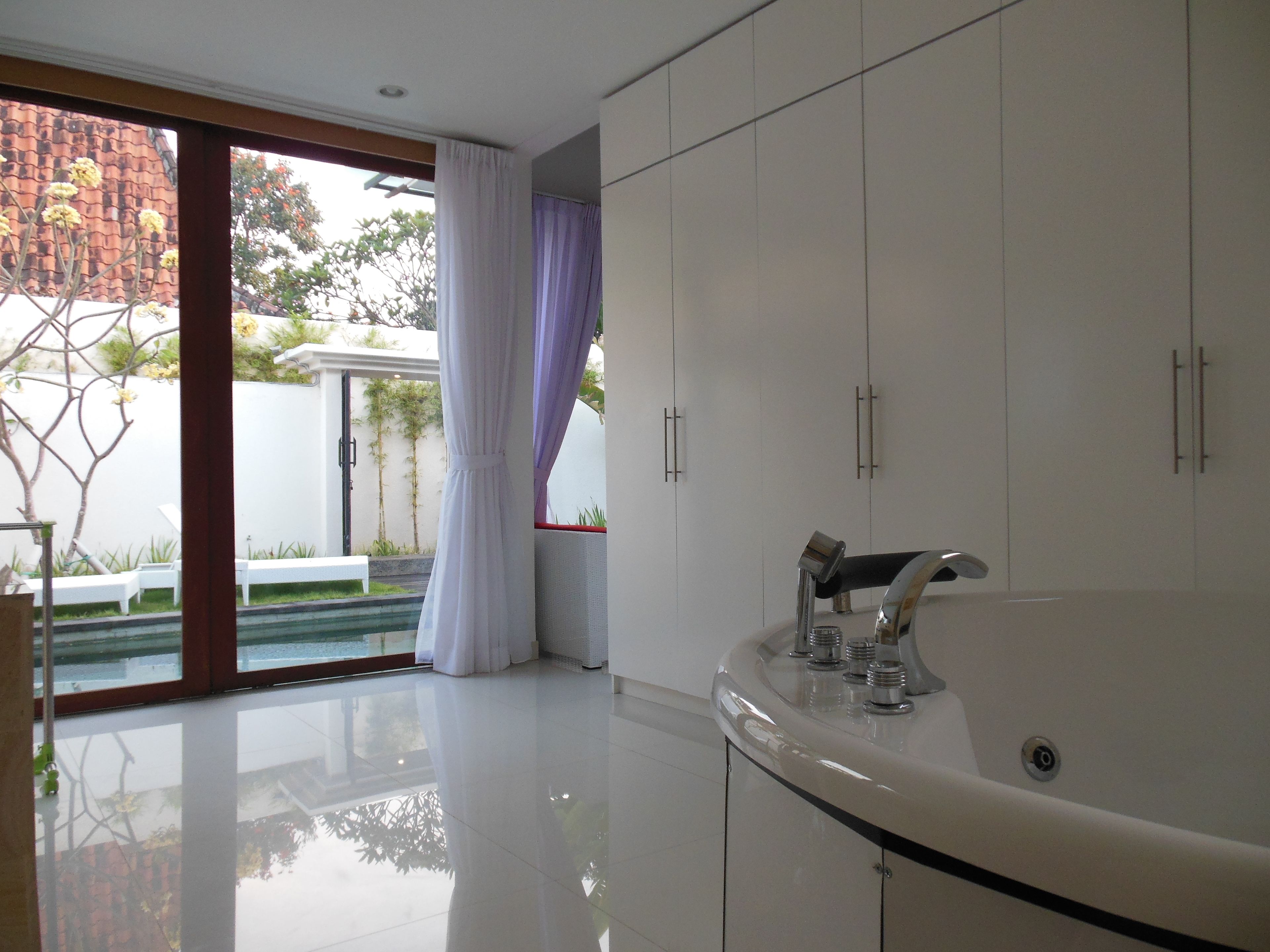 A modern bathroom with a large bathtub, white cabinets, and a glass door leading to a pool area.