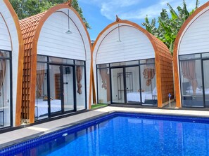 Un hôtel moderne doté d’une piscine, caractérisé par des structures en bois arquées et des portes en verre.