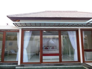Un espacio al aire libre techado con una cama y cortinas, techo de baldosas y puerta de vidrio.