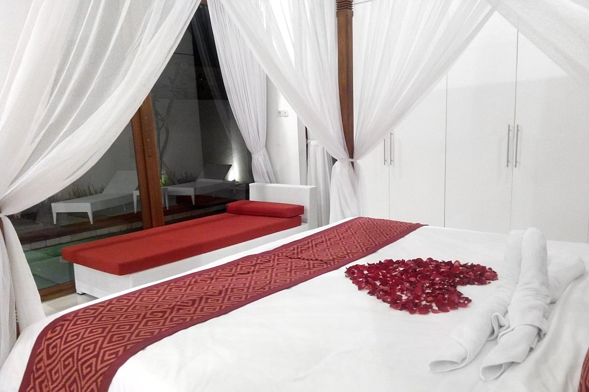 A bedroom with a large bed, a red sofa, and a canopy.