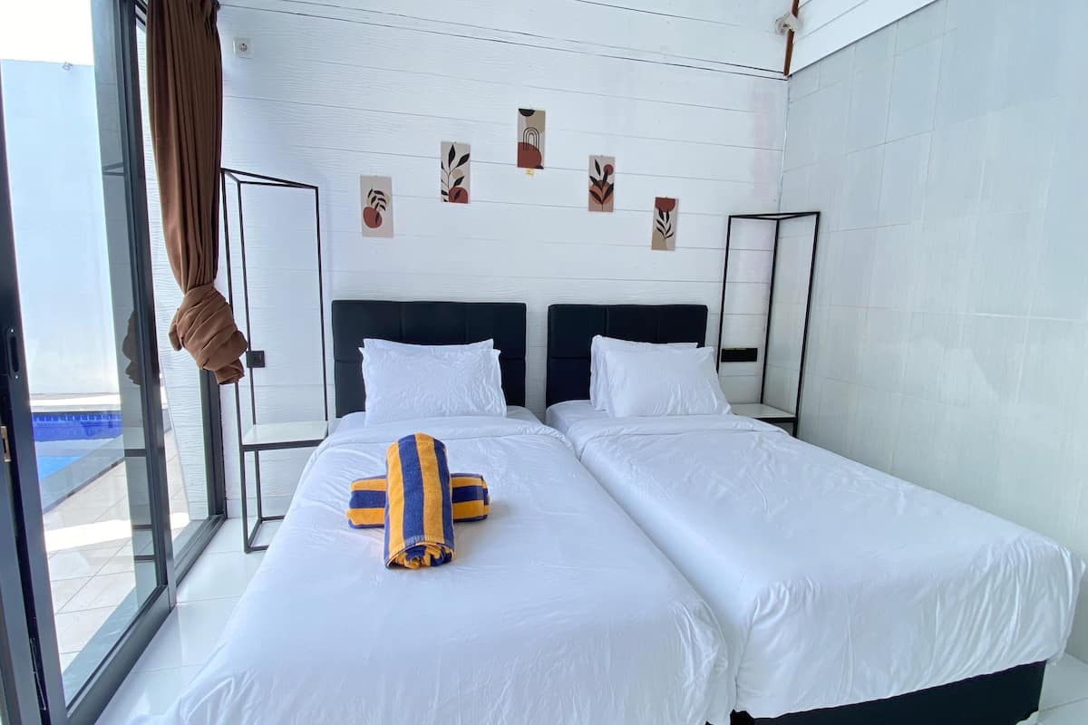 A hotel room with two beds, white bedding, a large window with curtains, and wall art.